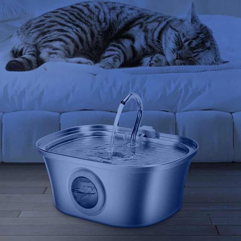 Bebedero en color azul con ventana retroiluminada, de noche junto a un gato dormido